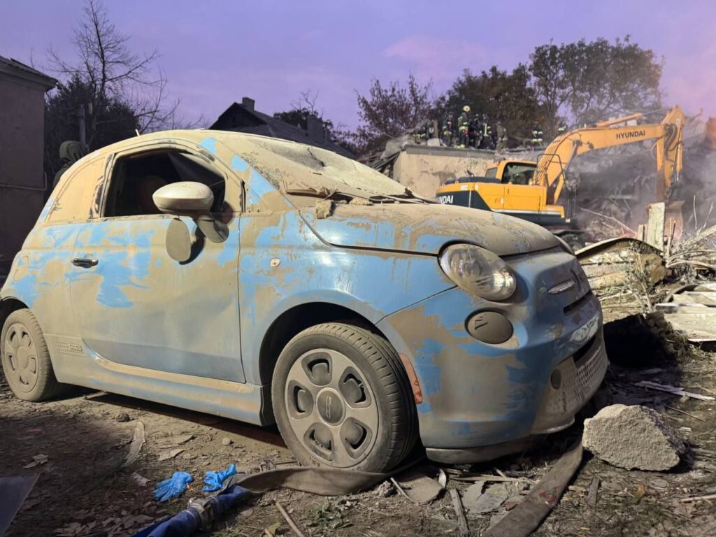 Пошкоджена автівка біля зруйнованого обстрілом будинку